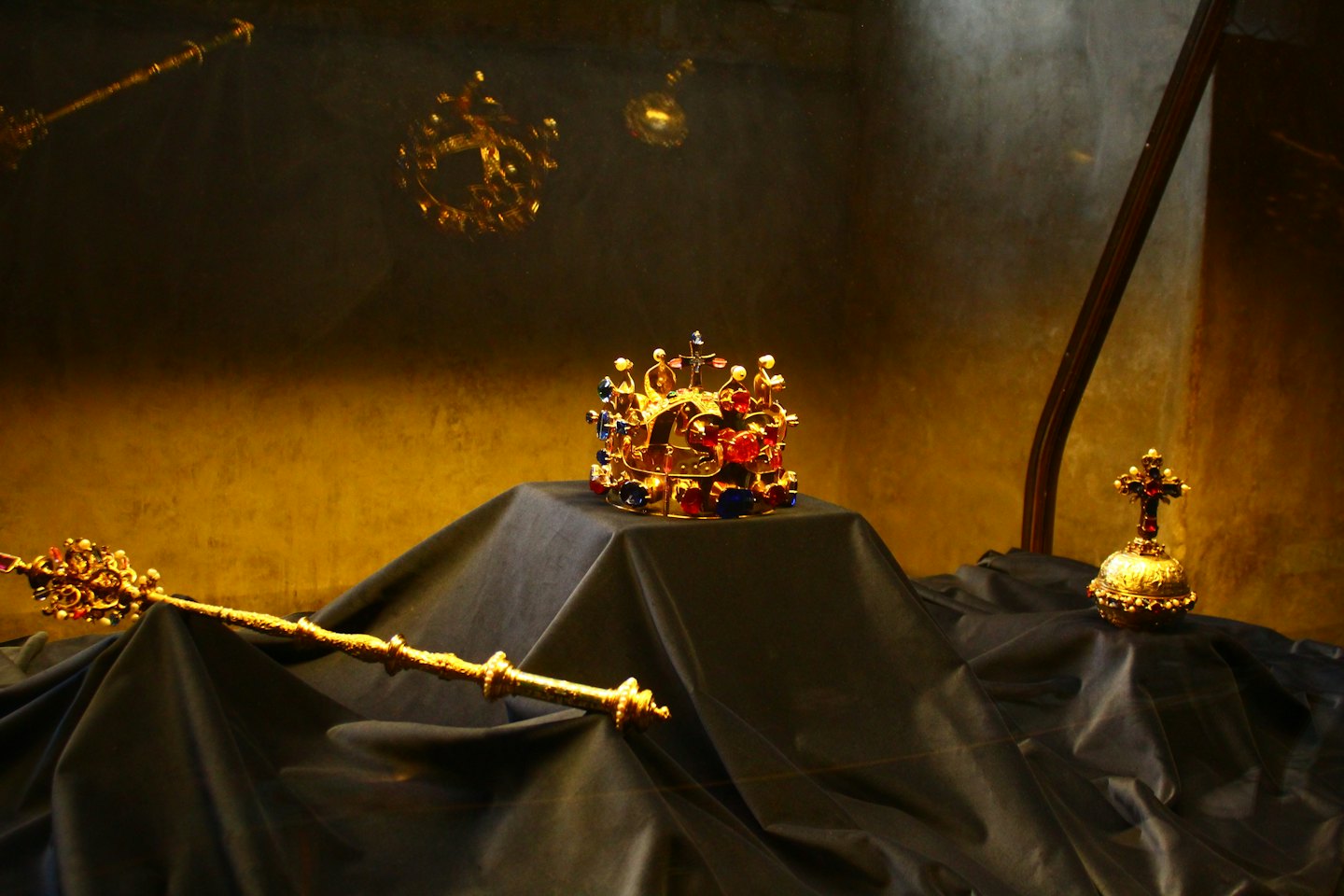 Ornate gold crown, scepter, and jeweled orb on a pedestal.