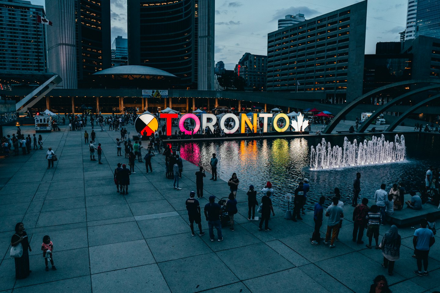 People gather around the Toronto sign at dusk in Nathan Phillips Square.